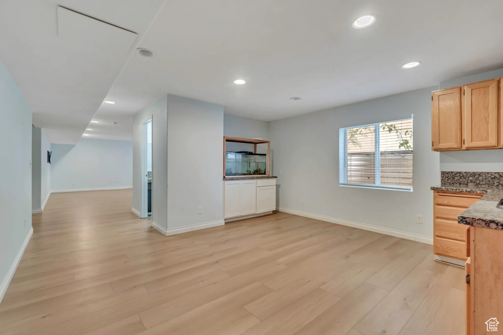 Basement kitchenette / dining area with light brown cabinets, recessed lighting, light wood-type flooring, and dark stone countertops