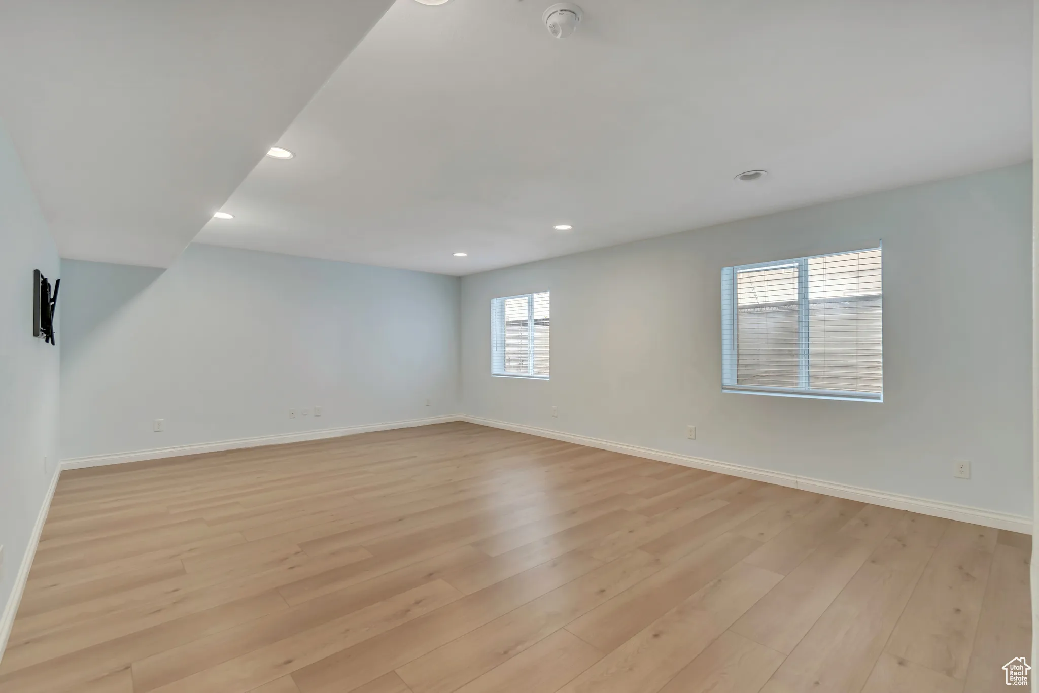 Basement living room with recessed lighting, light wood-style flooring, and stairway