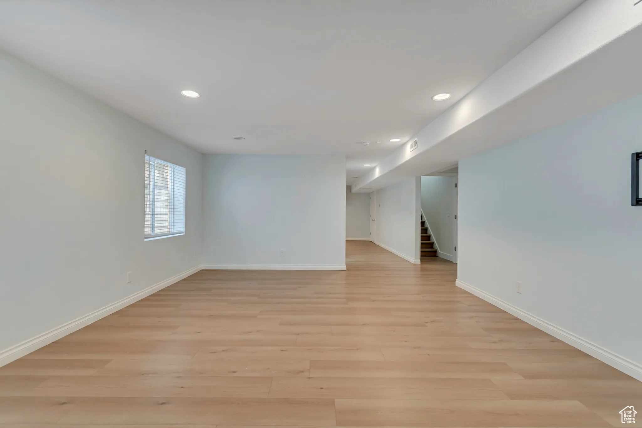 Basement living room with recessed lighting, light wood-style flooring, and stairway