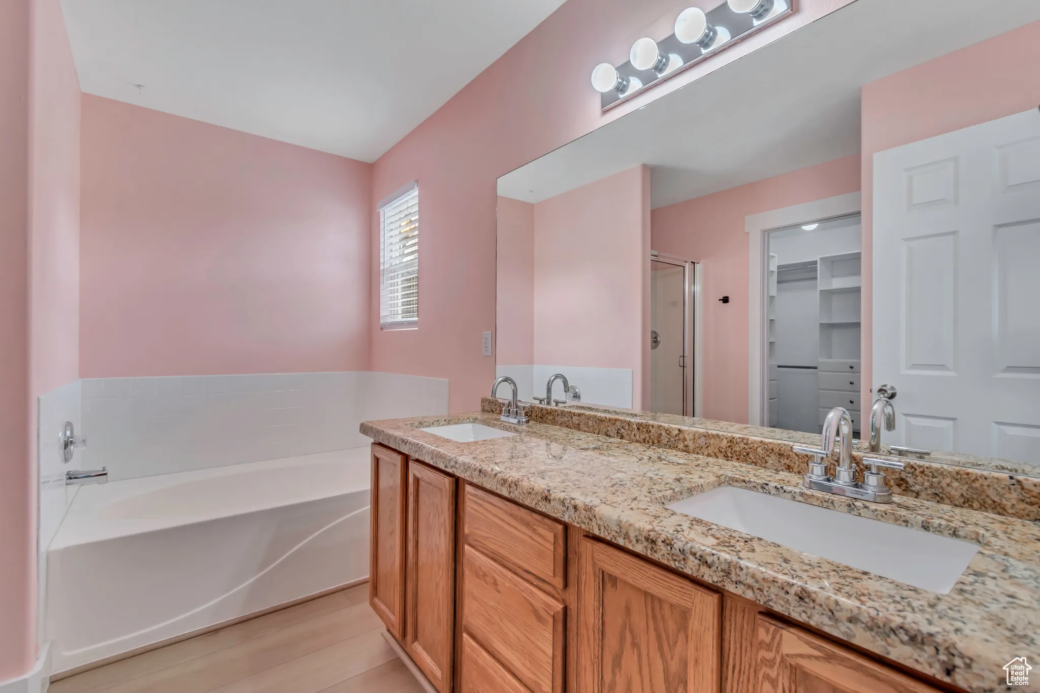 Primary full bath with a shower stall, double vanity, a bath, light wood-style flooring, and a spacious closet