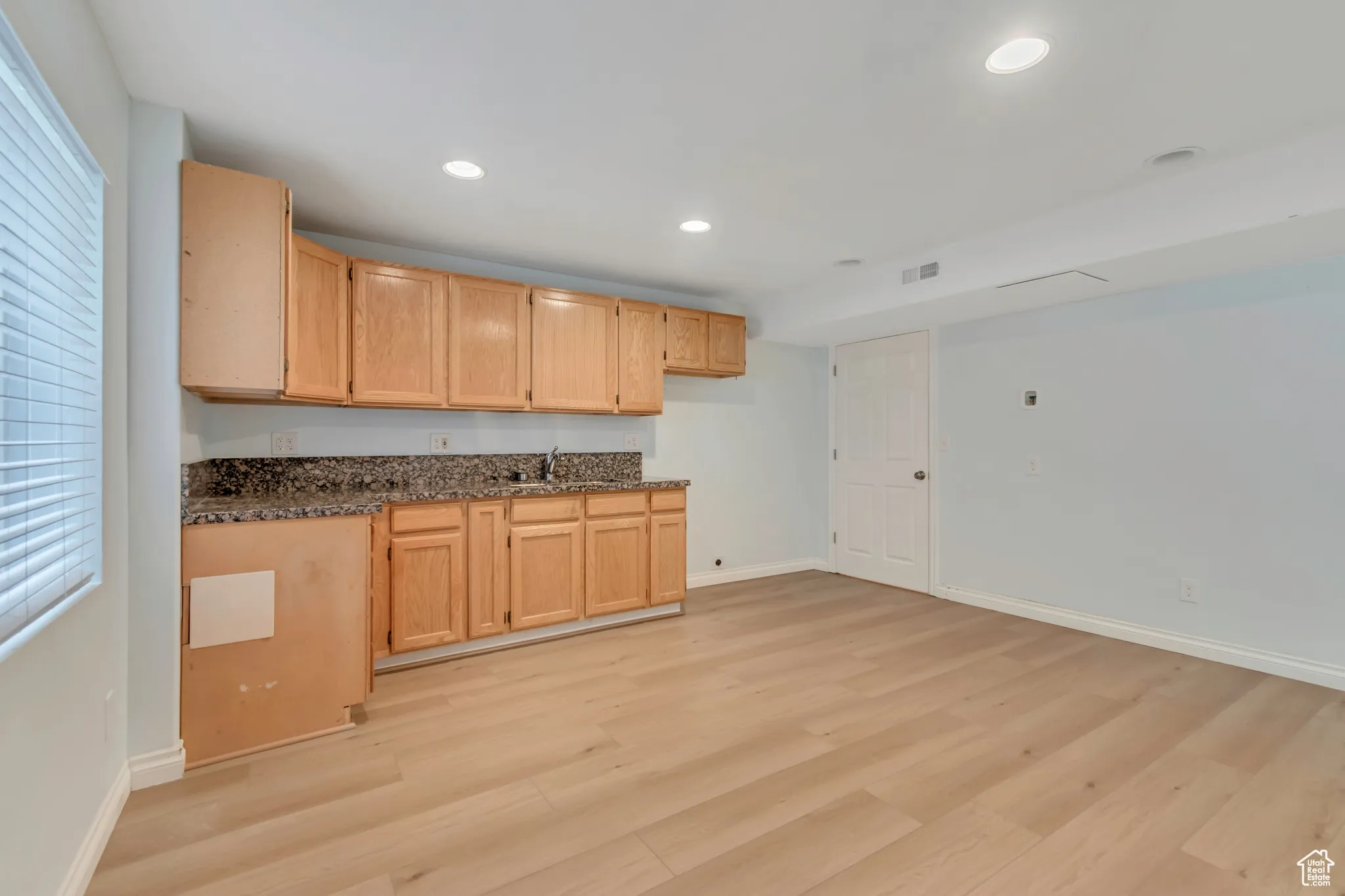 Basement kitchenette / dining area with light brown cabinets, recessed lighting, light wood-type flooring, and dark stone countertops