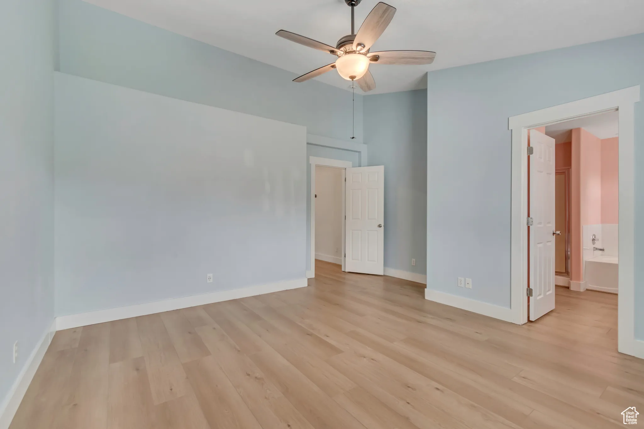 Primary bedroom with light wood-style floors, a ceiling fan, and ensuite bath