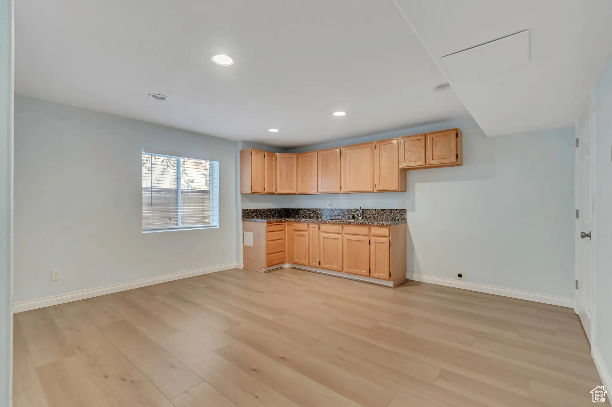 Basement kitchenette / dining area with light brown cabinets, recessed lighting, light wood-type flooring, and dark stone countertops