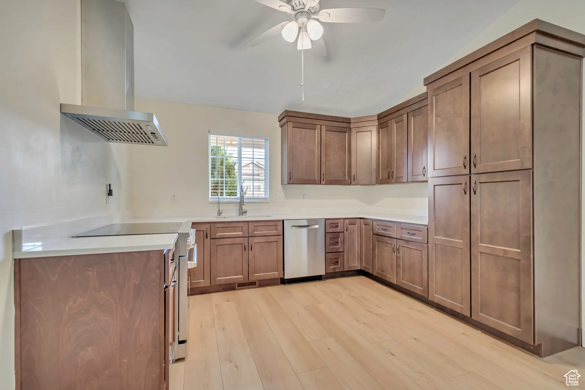 Kitchen with brown cabinetry, exhaust hood, light wood-style finished floors, appliances with stainless steel finishes, and ceiling fan