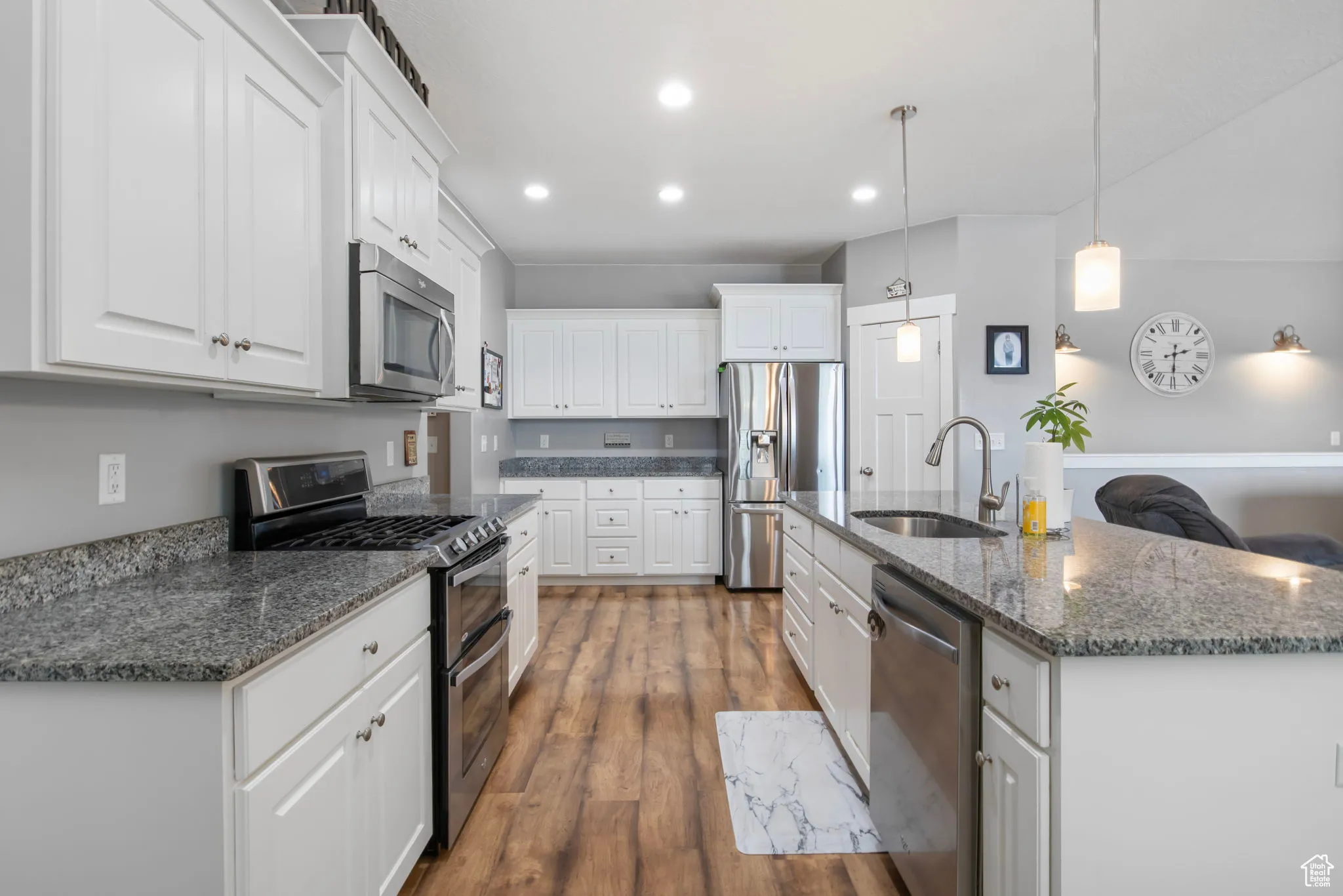 Kitchen featuring appliances with stainless steel finishes, dark finished floors, white cabinets, dark stone counters, and decorative light fixtures