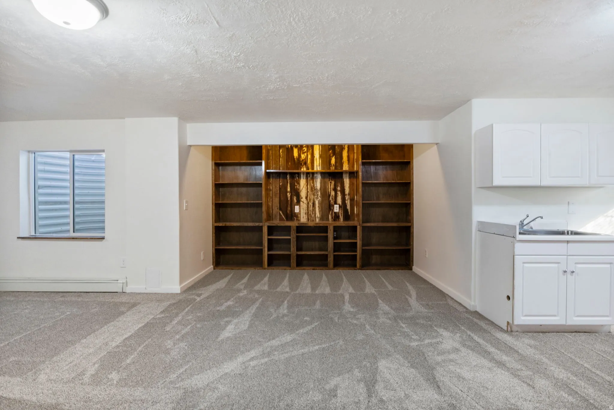 Unfurnished living room featuring light carpet, a baseboard radiator, and a textured ceiling