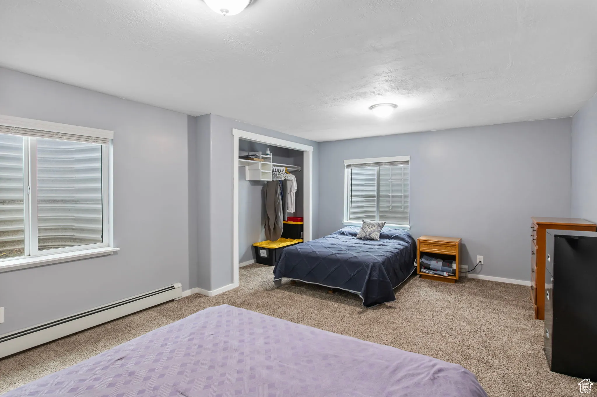 Bedroom with carpet flooring, a closet, baseboard heating, and a textured ceiling
