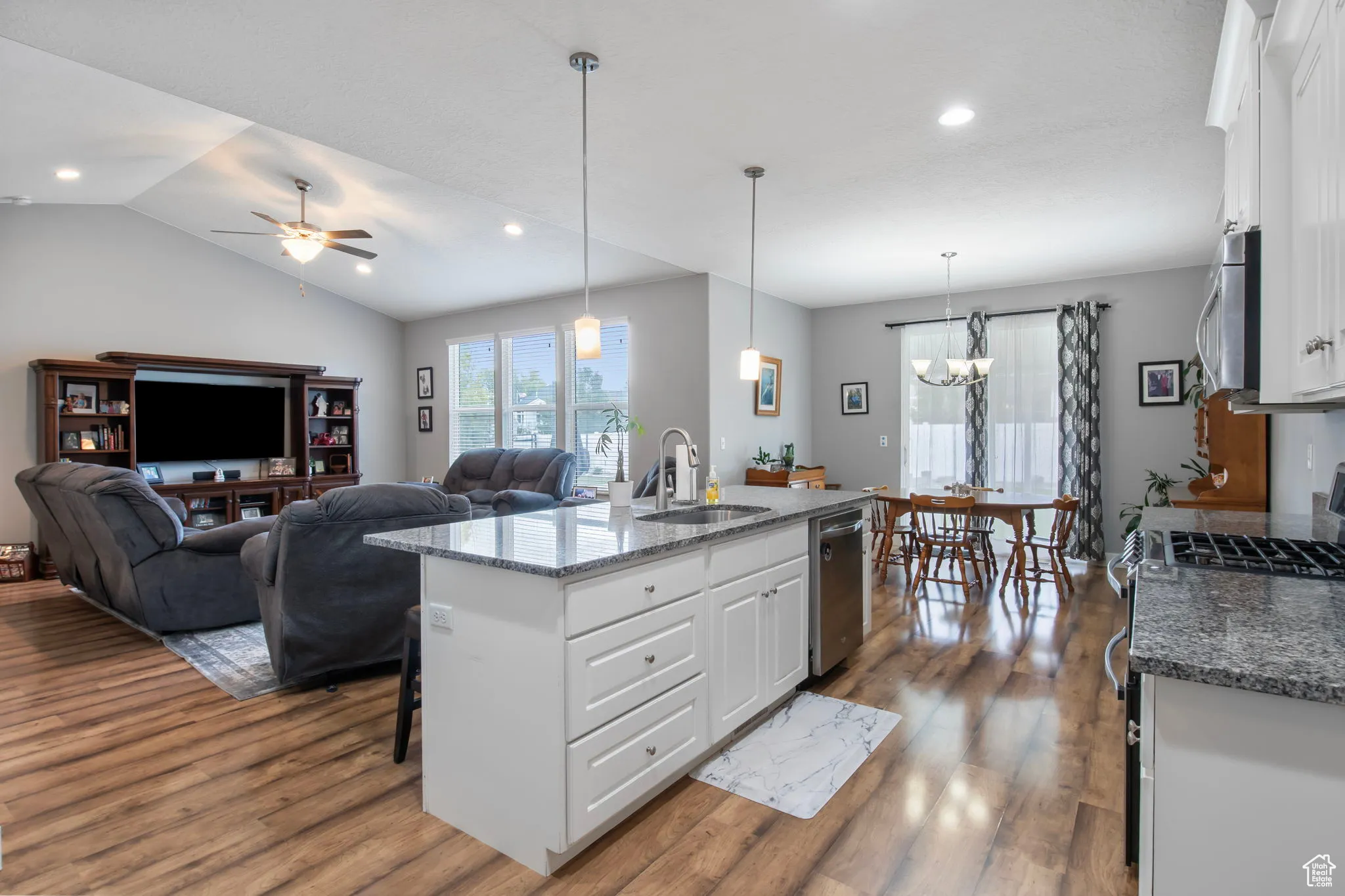 Kitchen featuring white cabinetry, dark stone counters, a center island with sink, decorative light fixtures, and a breakfast bar