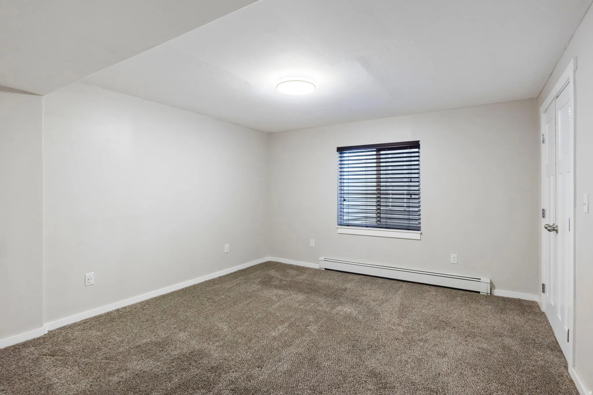 Empty room with baseboard heating and dark colored carpet