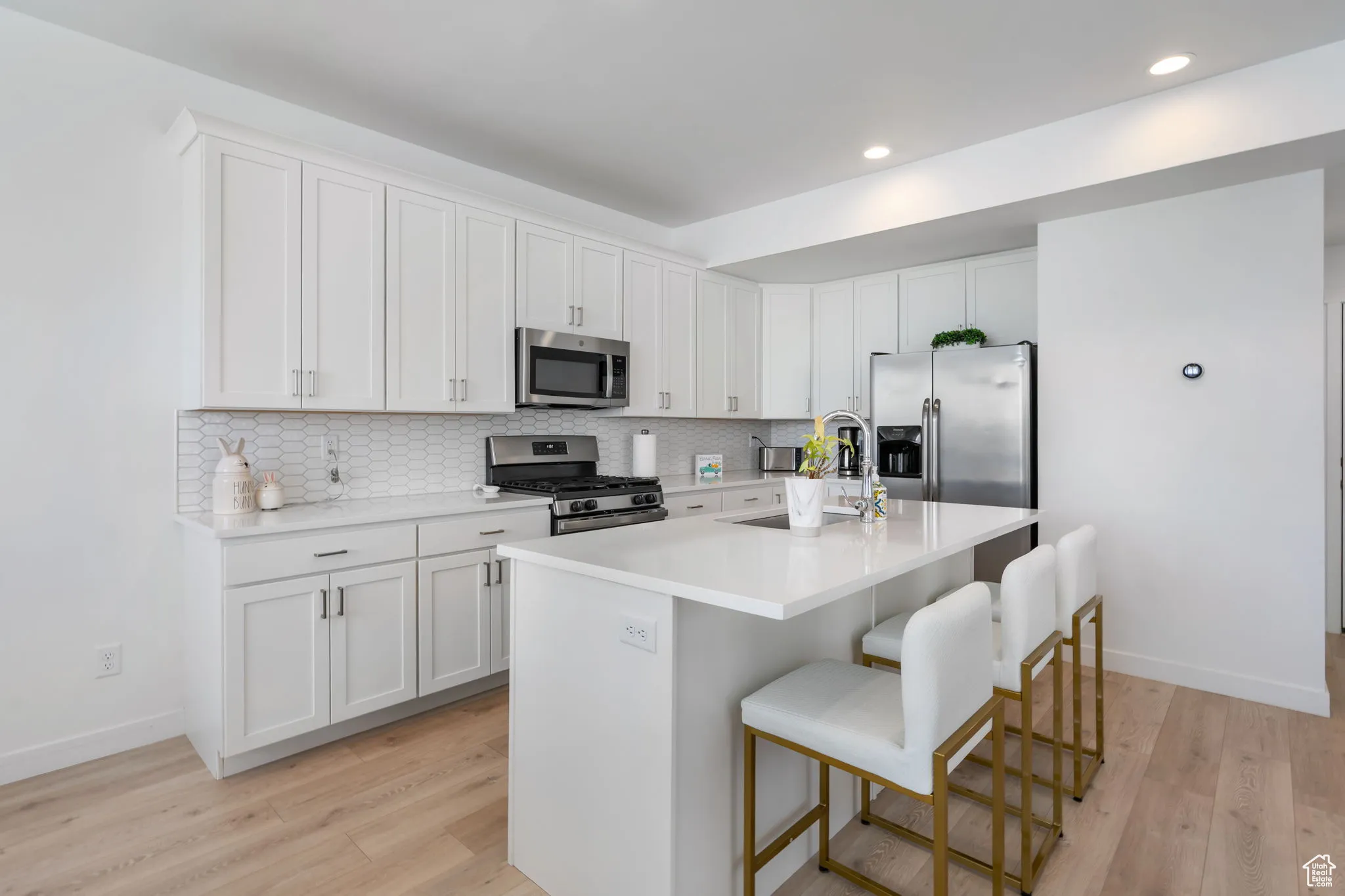 Kitchen featuring white cabinets, stainless steel appliances, an island with sink, a kitchen bar, and tasteful backsplash