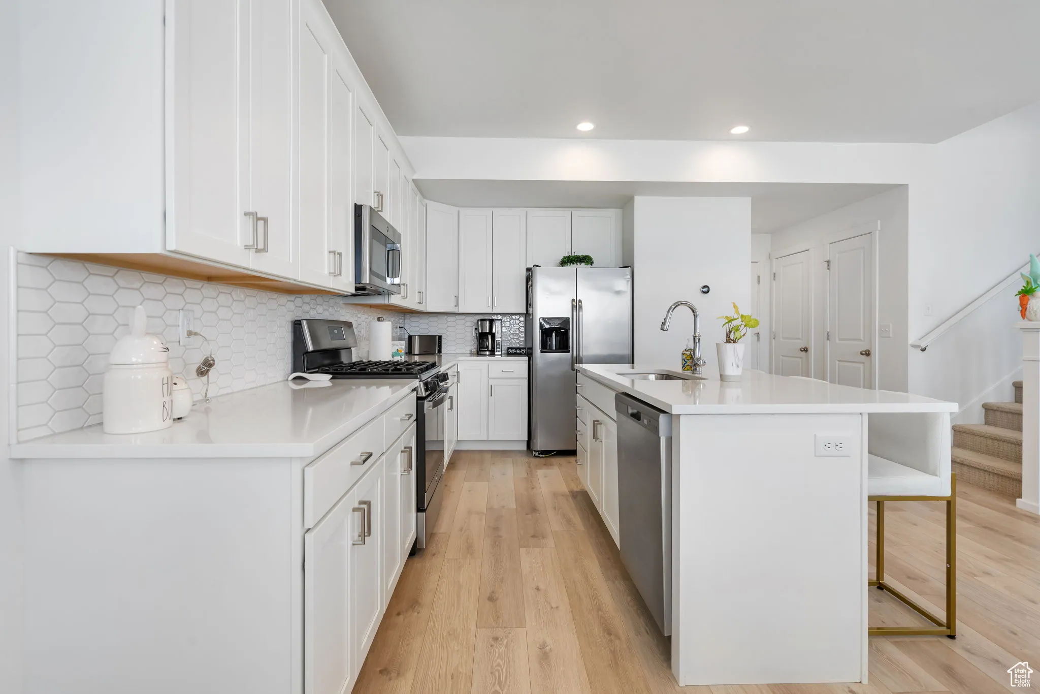Kitchen with appliances with stainless steel finishes, light wood finished floors, backsplash, a kitchen island with sink, and white cabinetry