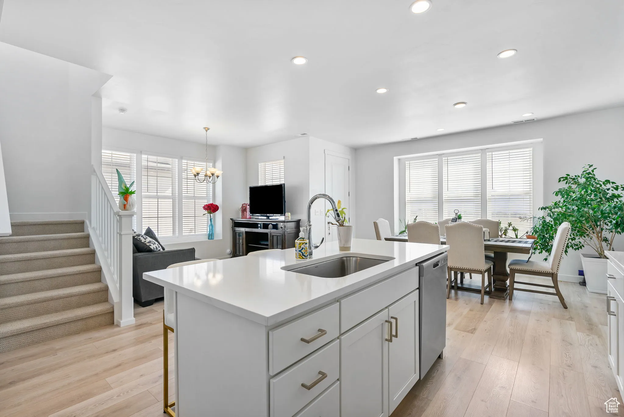 Kitchen featuring white cabinets, light wood finished floors, a kitchen island with sink, recessed lighting, and decorative light fixtures