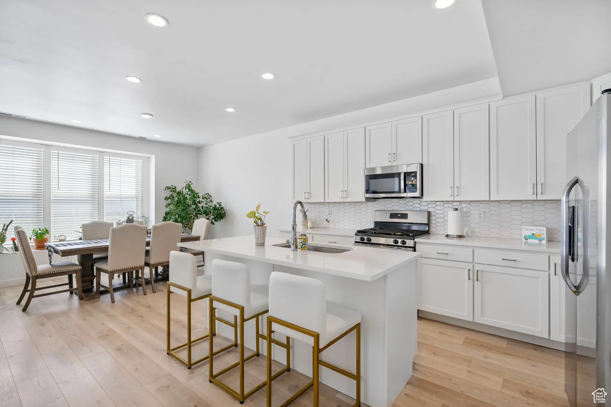 Kitchen with white cabinetry, an island with sink, a kitchen bar, recessed lighting, and appliances with stainless steel finishes