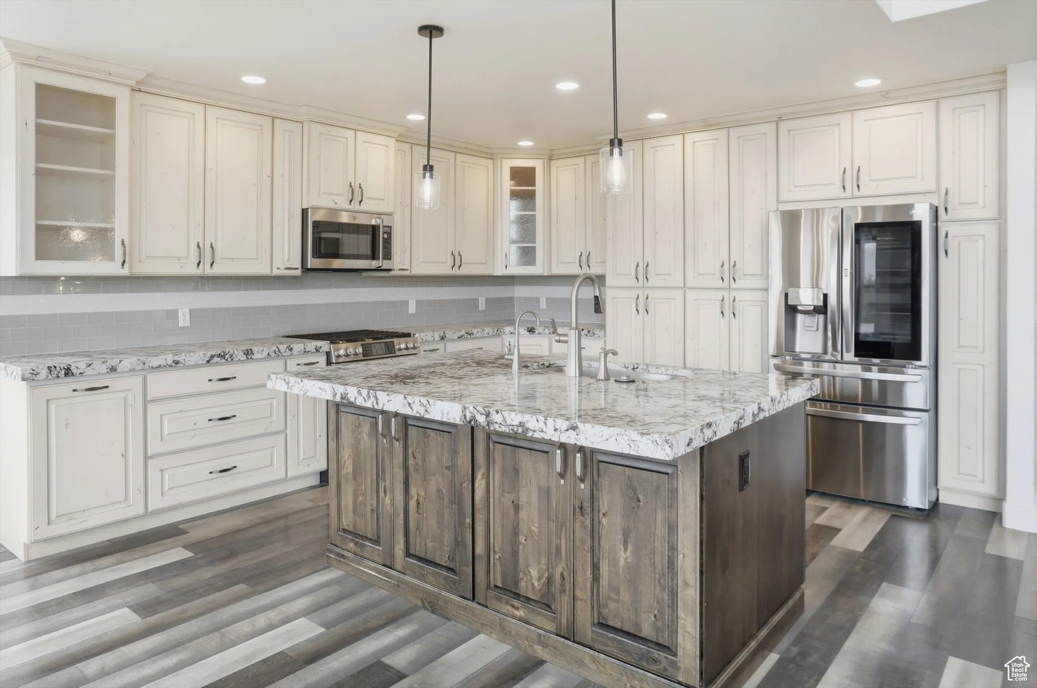 Kitchen featuring glass insert cabinets, stainless steel appliances, recessed lighting, a center island with sink, and light stone countertops