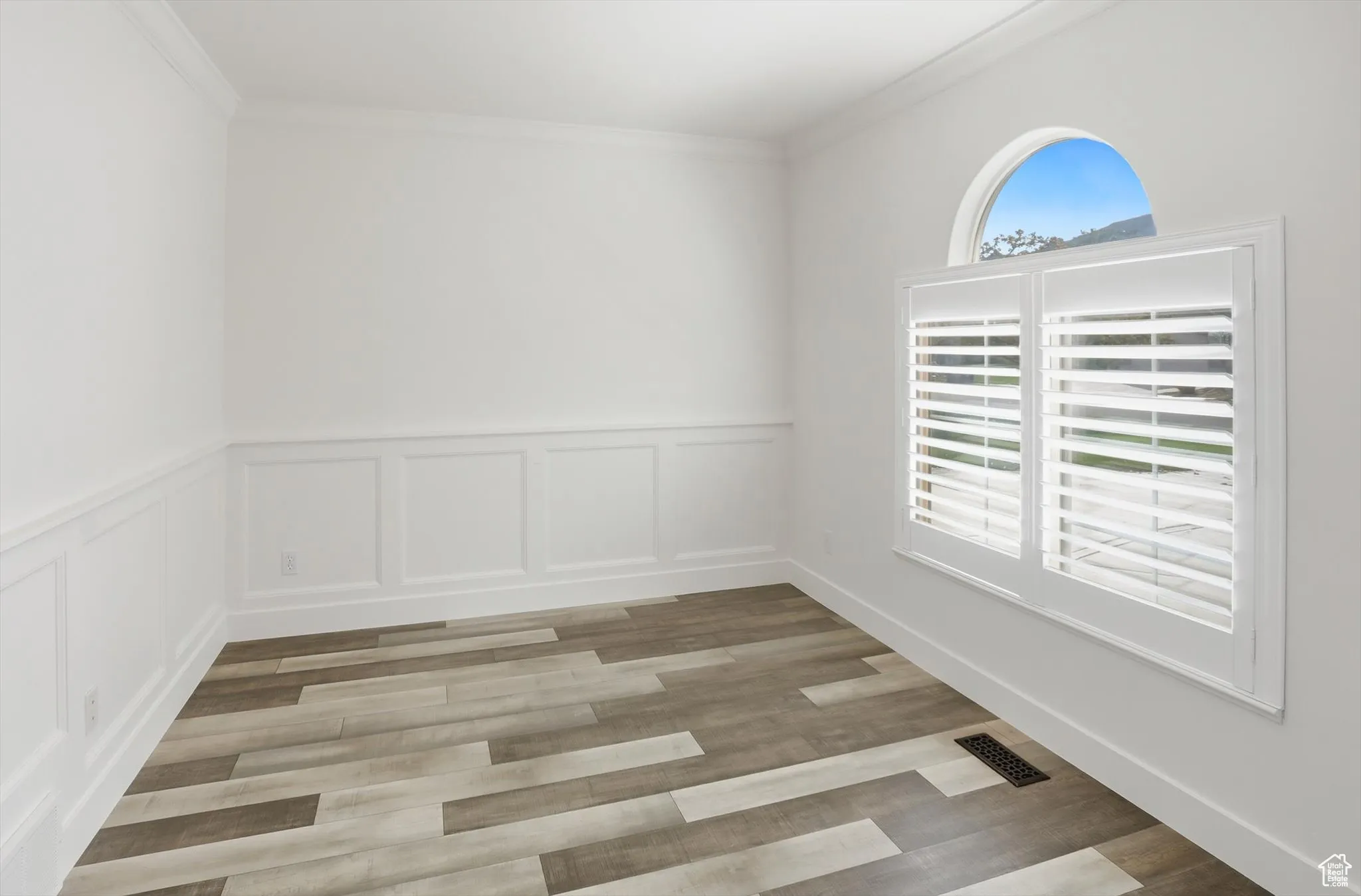 Spare room featuring a wainscoted wall, light wood-type flooring, a decorative wall, and ornamental molding