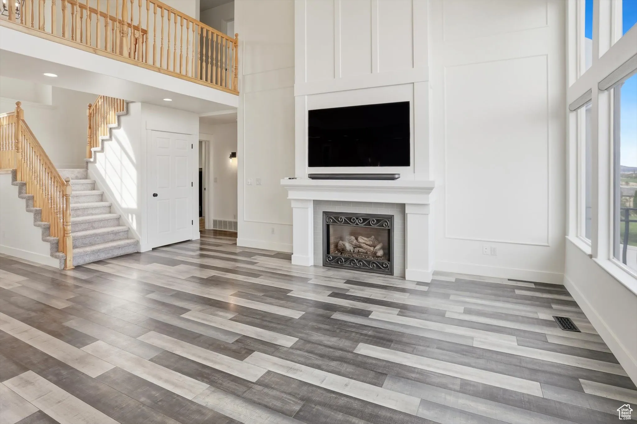 Unfurnished living room with a towering ceiling, a large fireplace, stairs, and light wood-style flooring