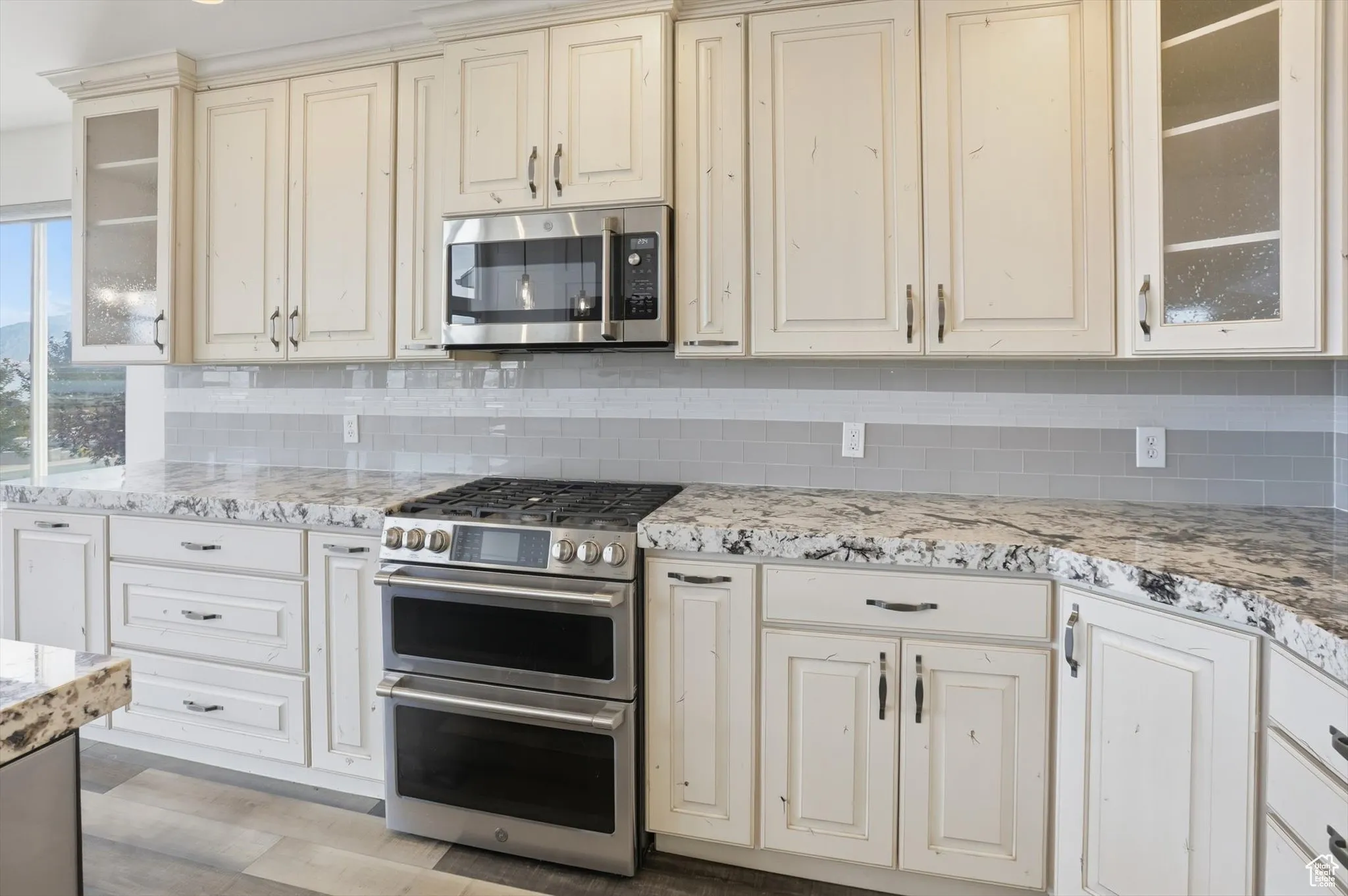Kitchen with glass insert cabinets, appliances with stainless steel finishes, tasteful backsplash, and cream cabinetry