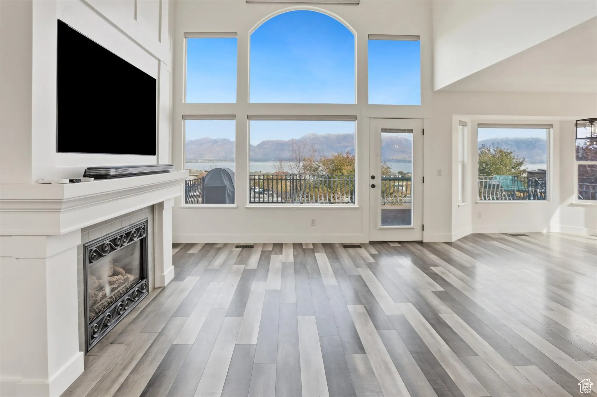 Unfurnished living room with a glass covered fireplace, light wood finished floors, and a towering ceiling