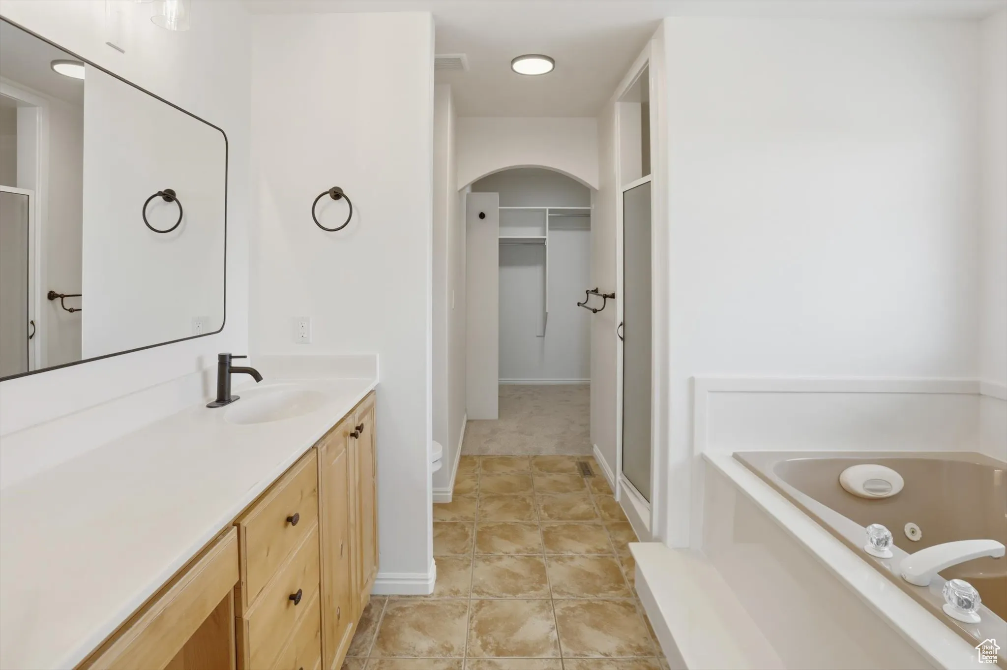 Bathroom featuring a tub with jets, vanity, a walk in closet, a stall shower, and light tile patterned flooring