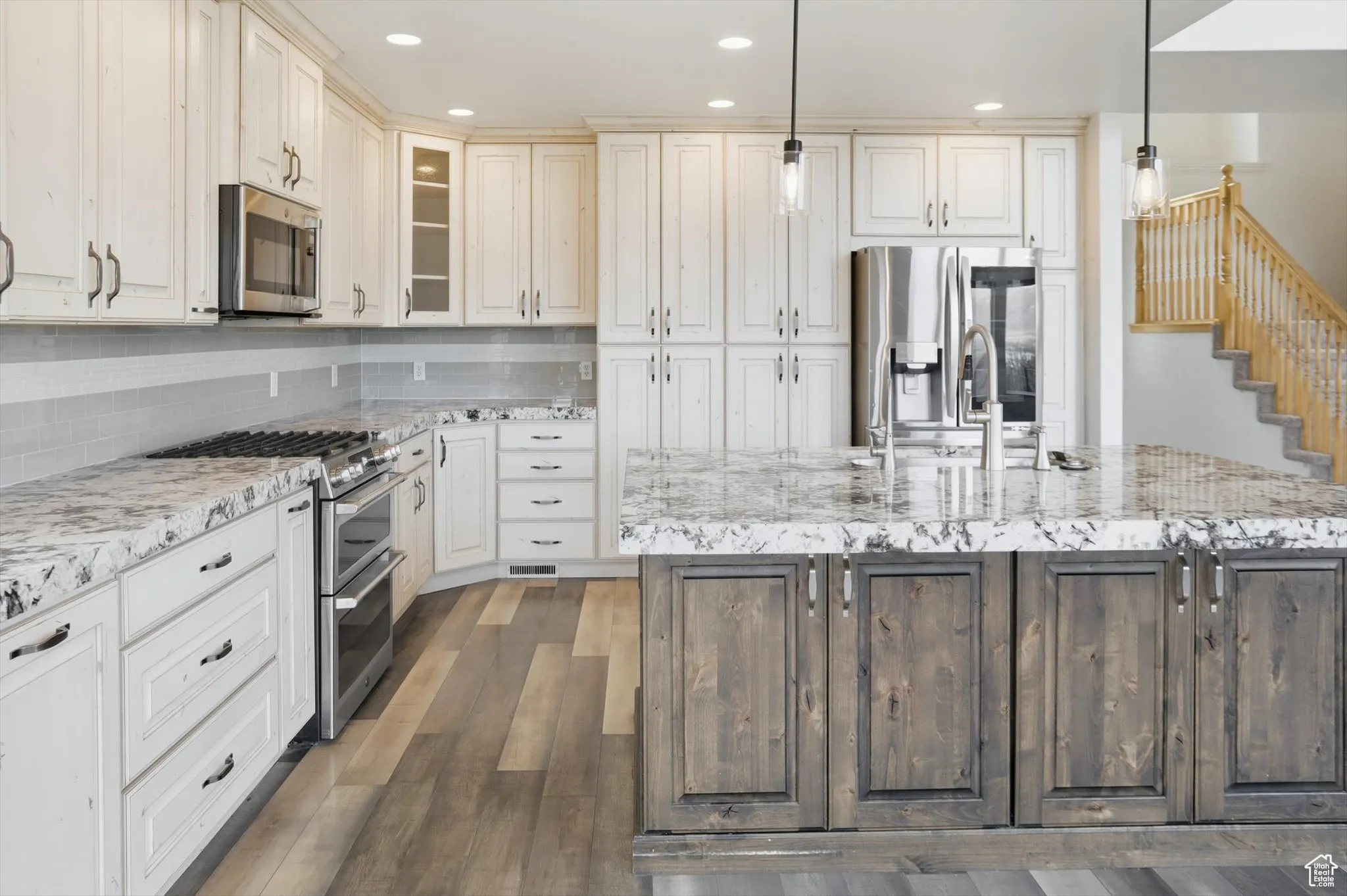 Kitchen with stainless steel appliances, glass insert cabinets, pendant lighting, light stone countertops, and recessed lighting