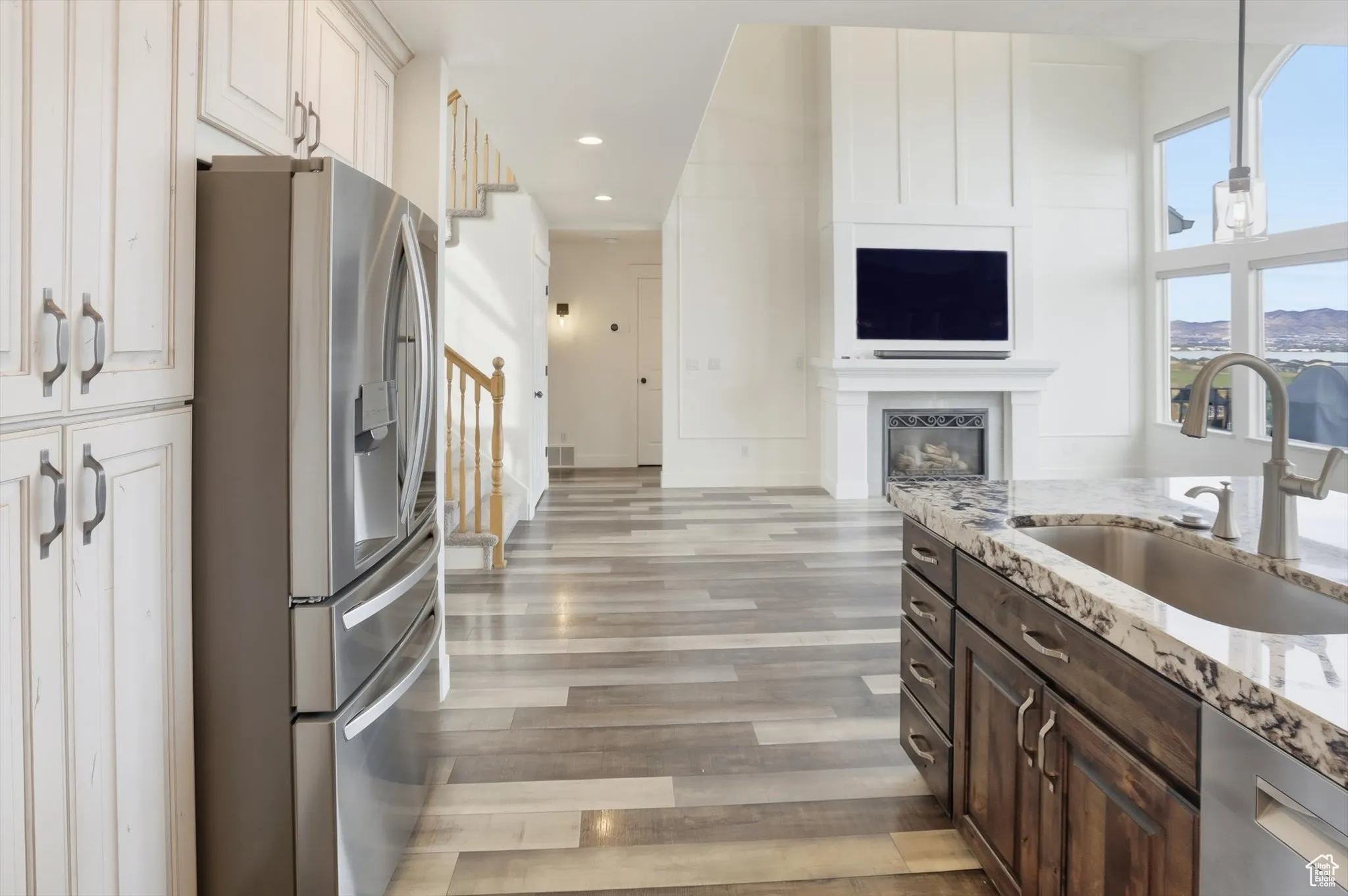 Kitchen featuring appliances with stainless steel finishes, dark brown cabinets, light stone countertops, a glass covered fireplace, and recessed lighting