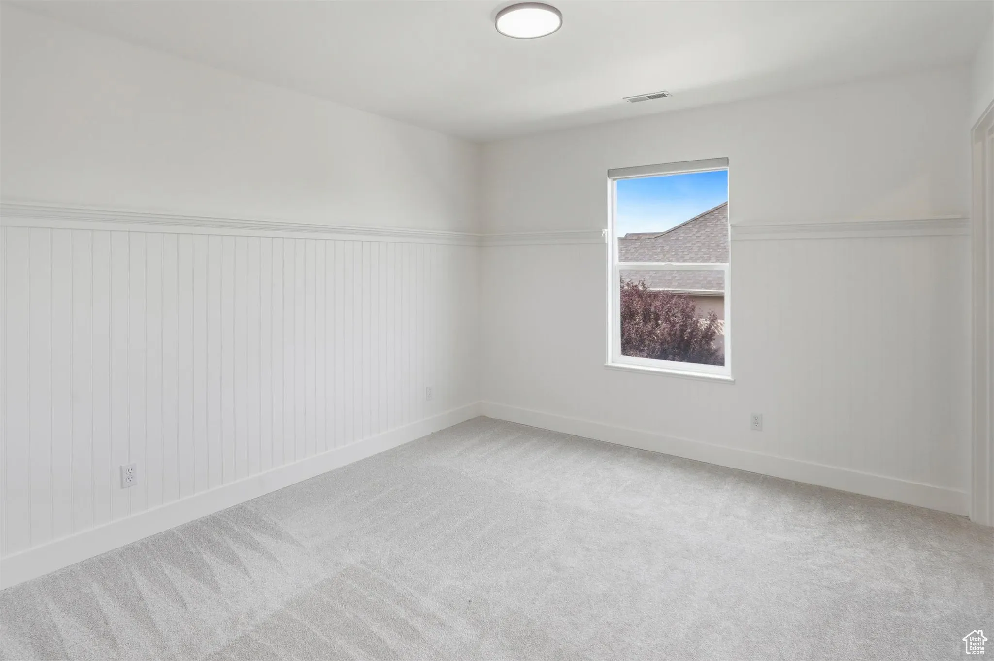 Carpeted spare room with a wainscoted wall and baseboards