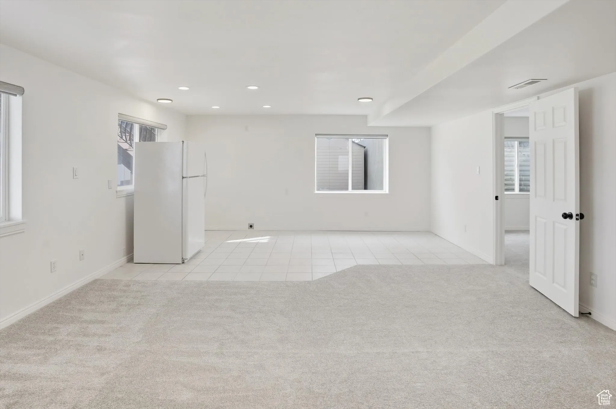 Unfurnished room featuring light tile patterned flooring, light colored carpet, plenty of natural light, and recessed lighting