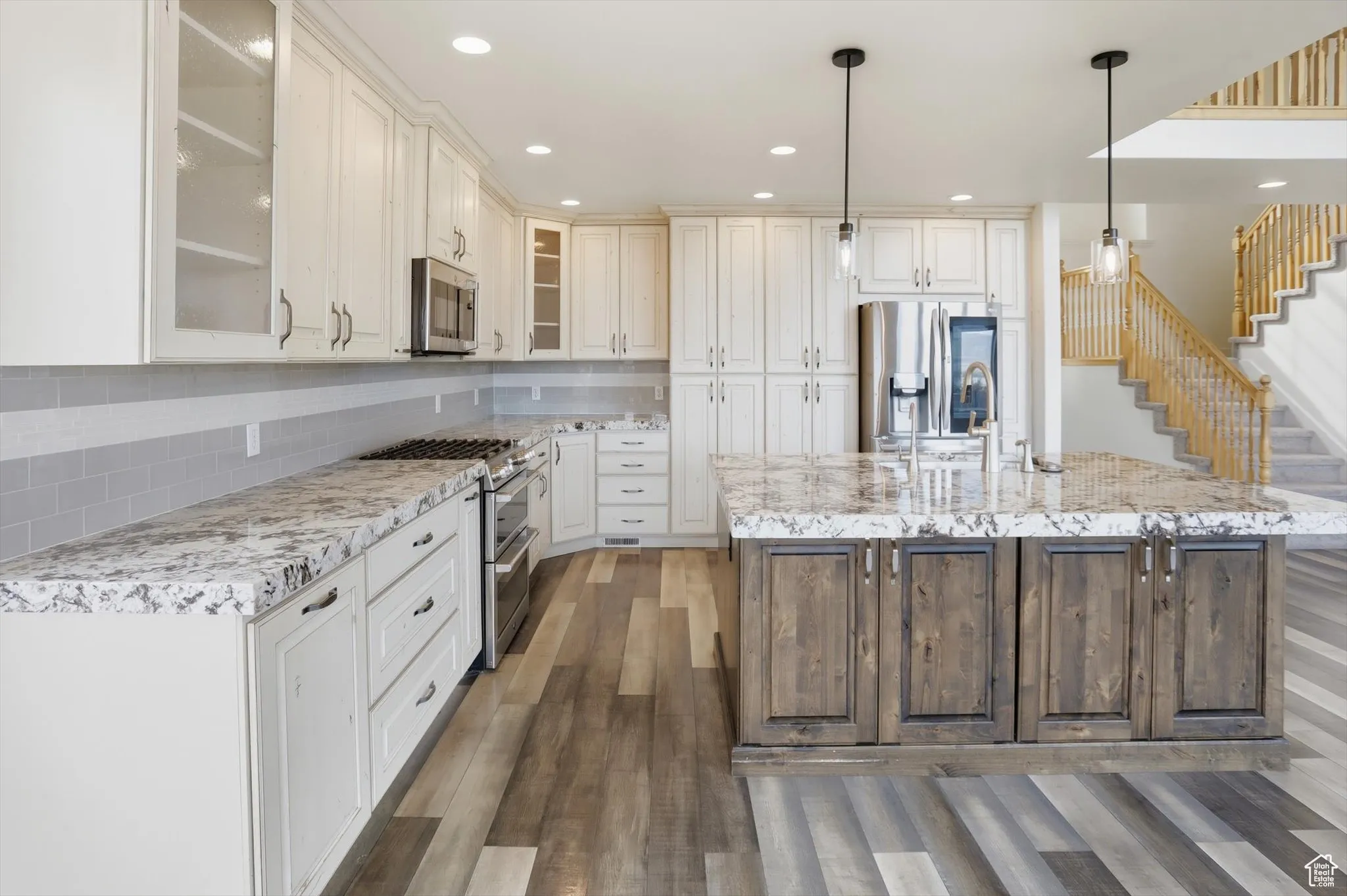Kitchen with stainless steel appliances, pendant lighting, recessed lighting, a center island with sink, and glass insert cabinets