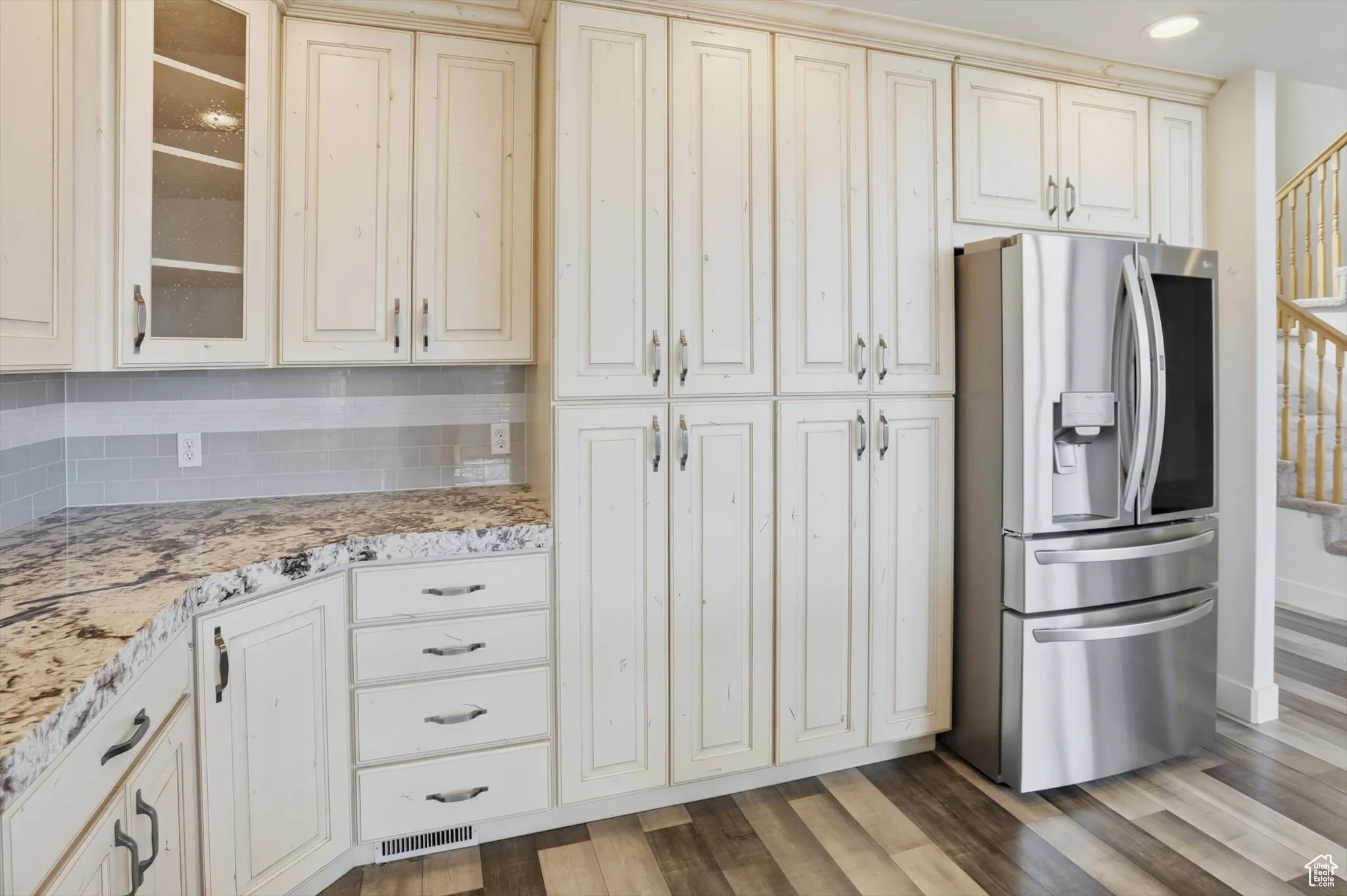 Kitchen with stainless steel fridge, tasteful backsplash, light stone counters, light wood-type flooring, and glass insert cabinets