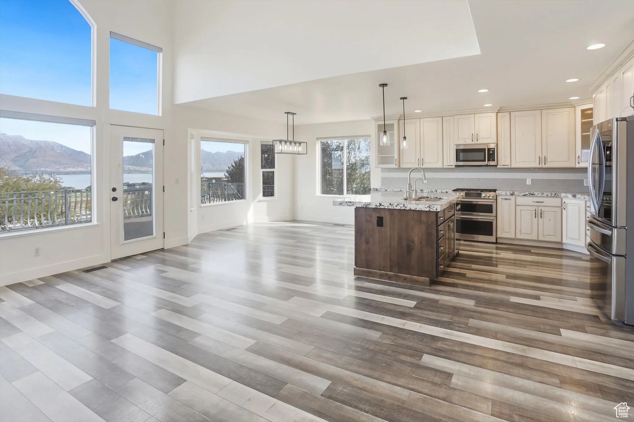 Kitchen with decorative light fixtures, stainless steel appliances, cream cabinetry, light stone counters, and dark brown cabinetry