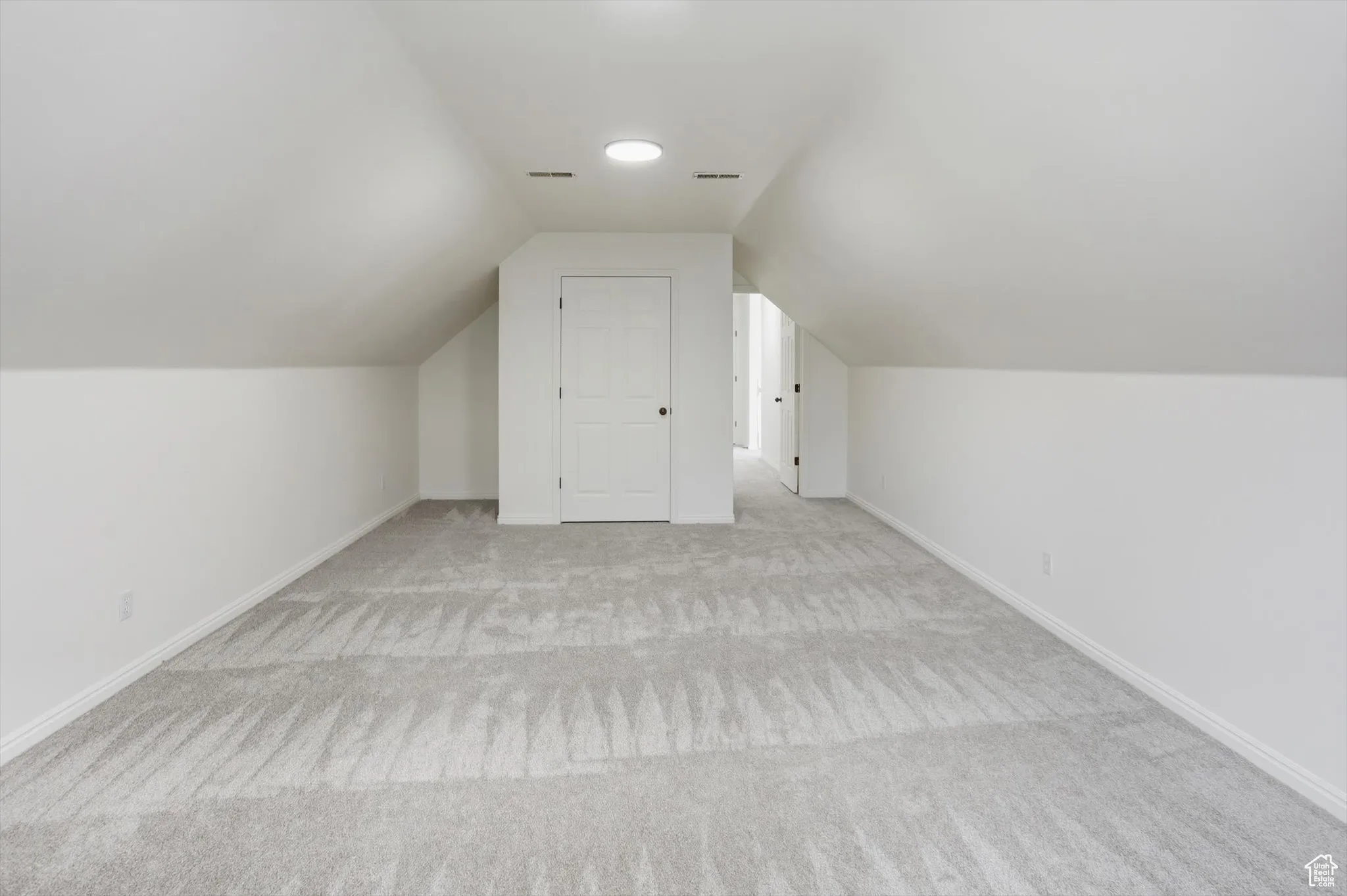 Bonus room with vaulted ceiling and light colored carpet
