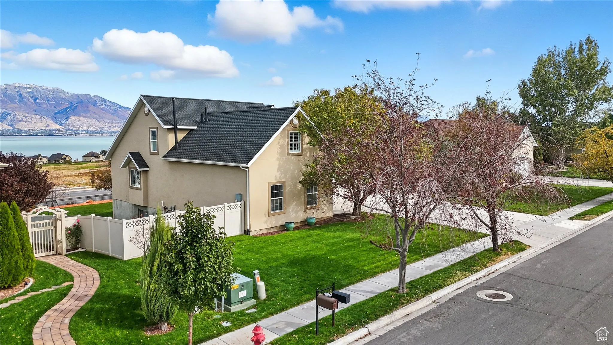 View of side of home with stucco siding, a gate, a water and mountain view, and roof with shingles