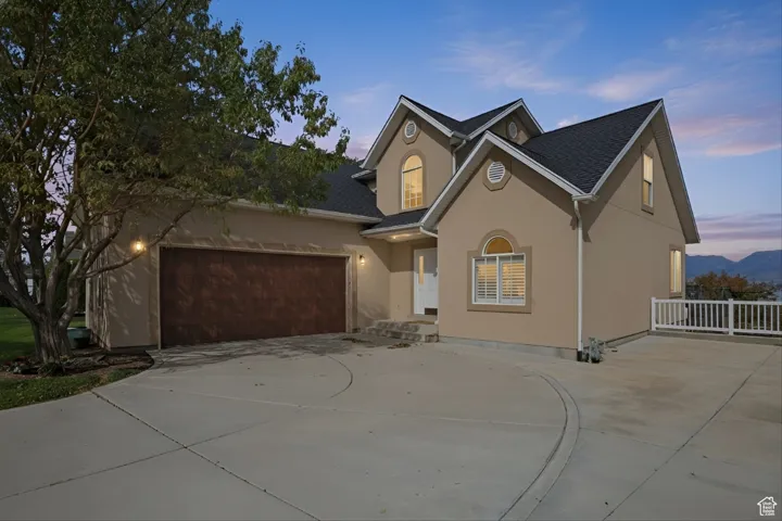 Traditional home with stucco siding, driveway, a shingled roof, and a garage