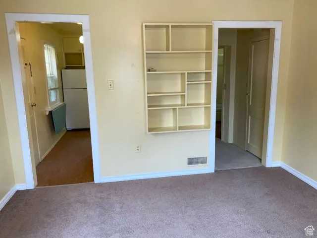 Unfurnished bedroom featuring carpet flooring and freestanding refrigerator