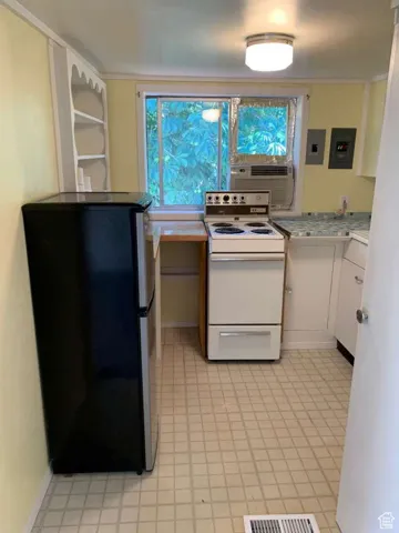 Kitchen with white range with electric cooktop, light countertops, freestanding refrigerator, white cabinetry, and cooling unit