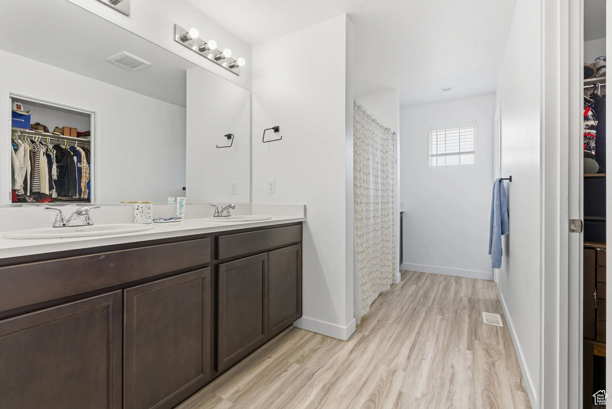 Full bath featuring a walk in closet, double vanity, a shower with curtain, and light wood-type flooring