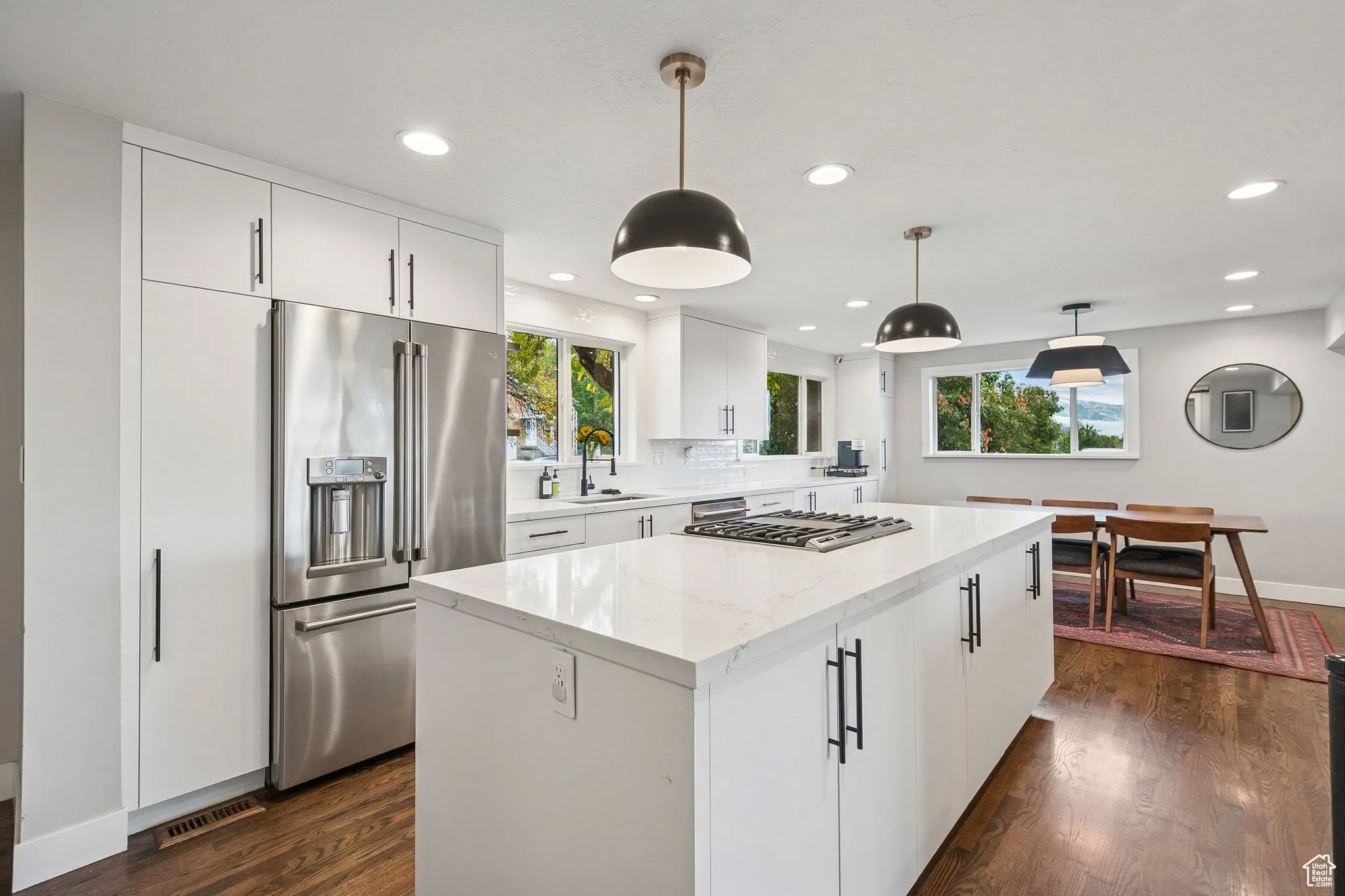 Kitchen featuring hanging light fixtures, white cabinetry, stainless steel appliances, a kitchen island, and dark wood-style flooring