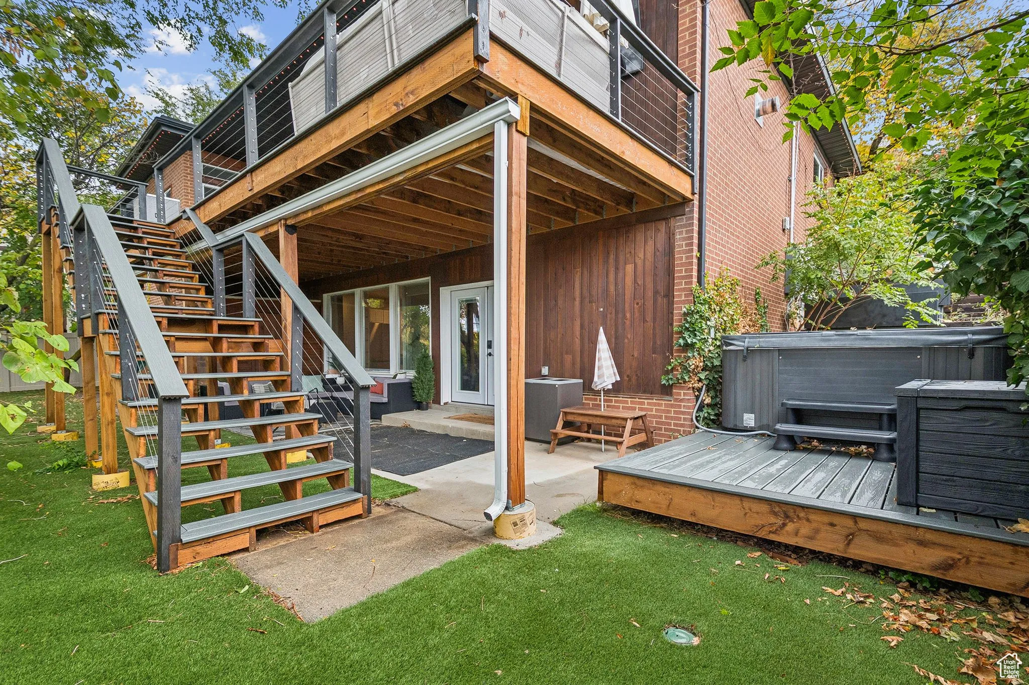 Back of house featuring a wooden deck, stairway, a patio area, a hot tub, and a yard