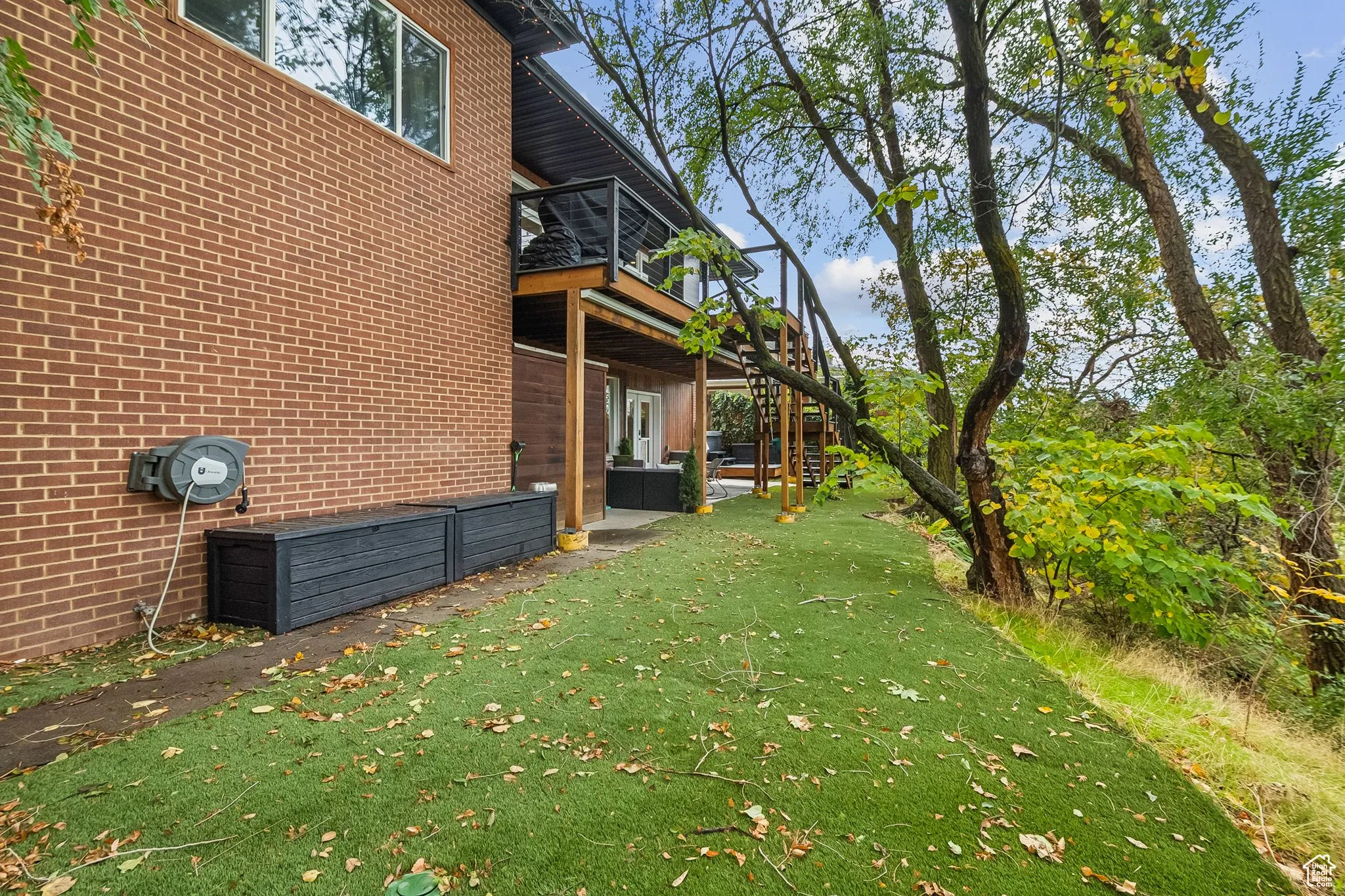 View of home's exterior featuring a patio area, a yard, brick siding, a deck, and stairway