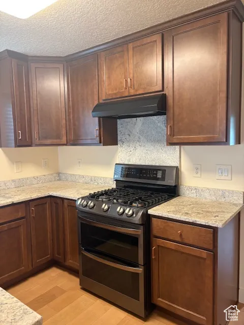 Kitchen featuring range with two ovens, light stone counters, light wood-style flooring, under cabinet range hood, and a textured ceiling