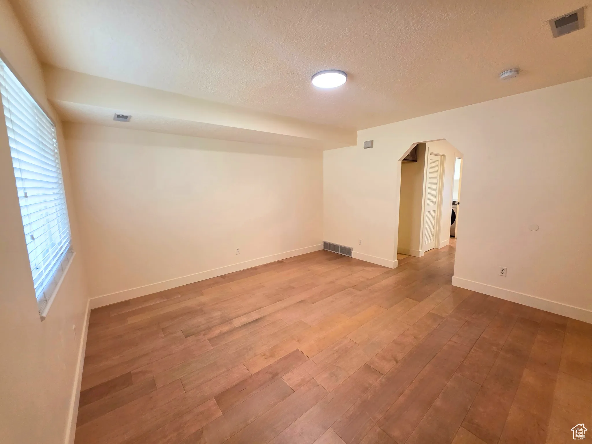 Empty room featuring arched walkways, a textured ceiling, and light wood-style floors