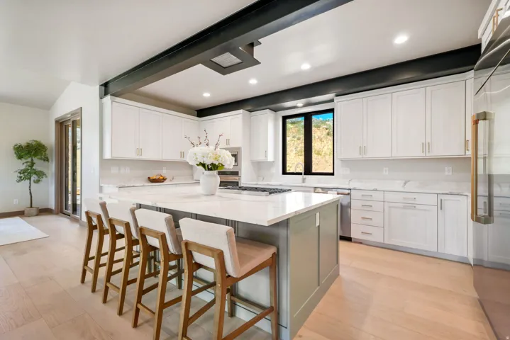 Bright kitchen featuring a large central island with seating, white shaker cabinetry, stainless steel appliances, and light wood-finish flooring