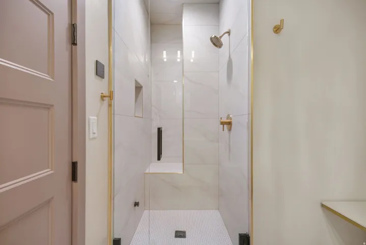 Tiled shower with glass enclosure, gold-finish fixtures, built-in bench, and recessed shelf