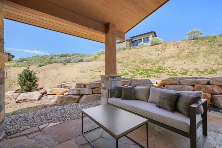 Covered patio with a wood-plank ceiling, stone paver flooring, and a stone-clad structural column