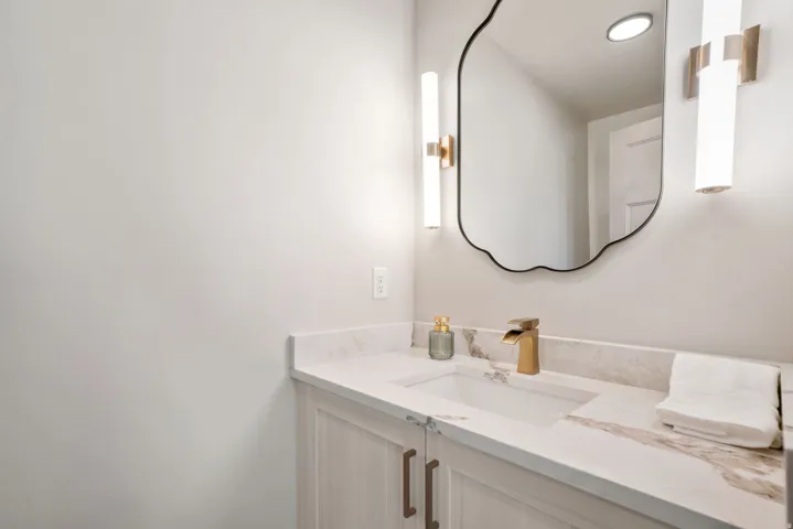 White vanity with light wood-finish cabinetry, a white countertop with brown veining, and a rectangular undermount sink