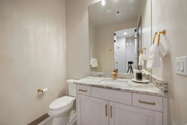 White vanity with gold hardware, integrated rectangular sink, and stone-finish countertop with matching backsplash