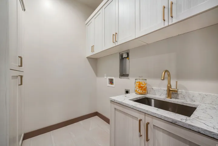 Utility room featuring wood-finish flooring, white cabinetry with bronze hardware, a white countertop with grey veining, a stainless steel undermount sink, and a gold-tone faucet