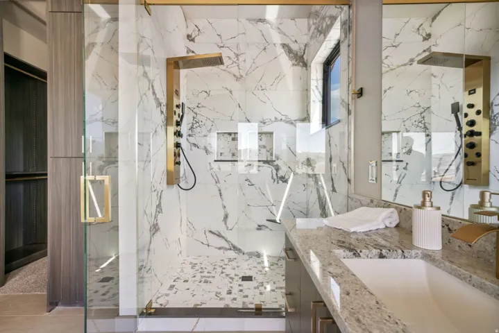 Glass-enclosed shower with gold-tone fixtures, full-height marble-patterned tile, and a mosaic tile floor