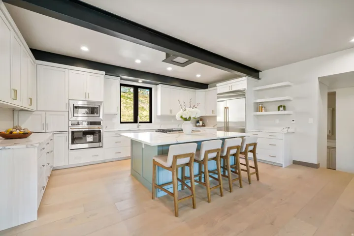 Contemporary kitchen featuring a light wood-finish floor, white cabinetry, a built-in oven and microwave, and a large center island with a light blue base and a white countertop