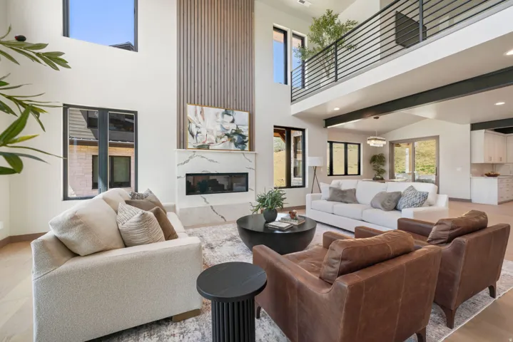 Two-story great room with a linear fireplace set into a large-format veined stone surround, vertical wood accent paneling, and an upper-level balcony featuring horizontal metal railings